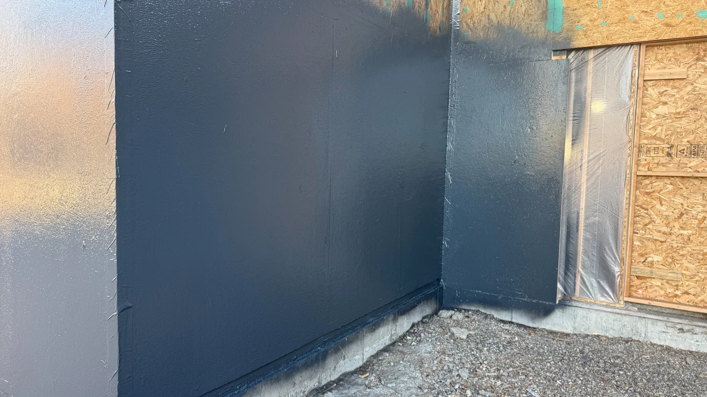 Spray-applied black waterproofing membrane on a new Montana foundation wall before backfill